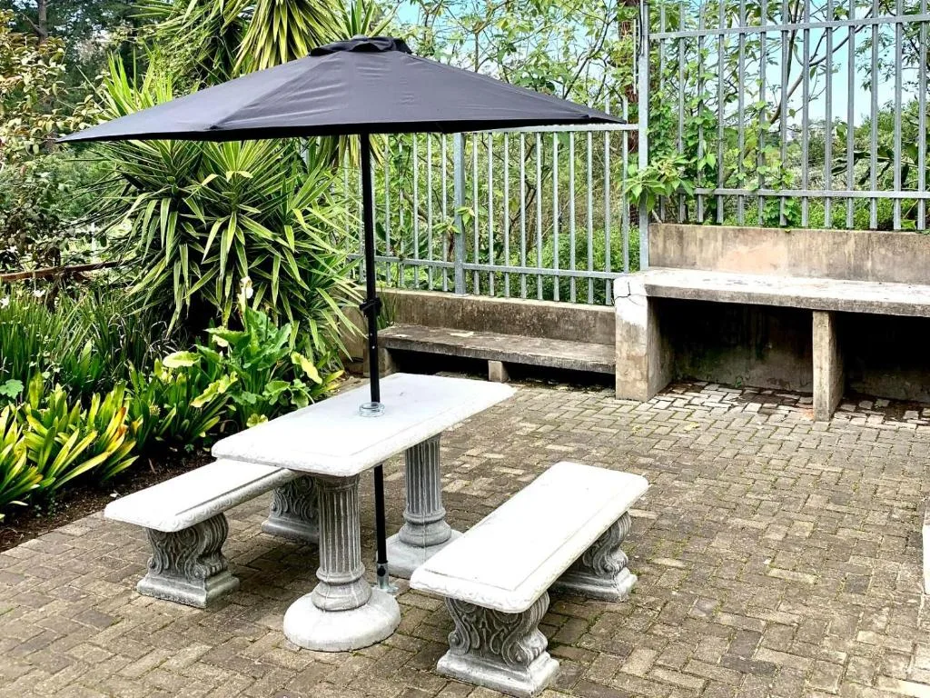 Outdoor patio with picnic table, black umbrella, and lush garden vegetation