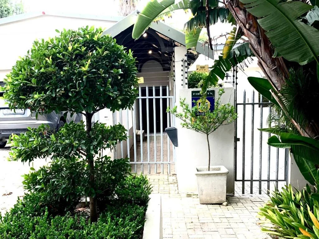 White cottage entrance with lush tropical plants and black security gate