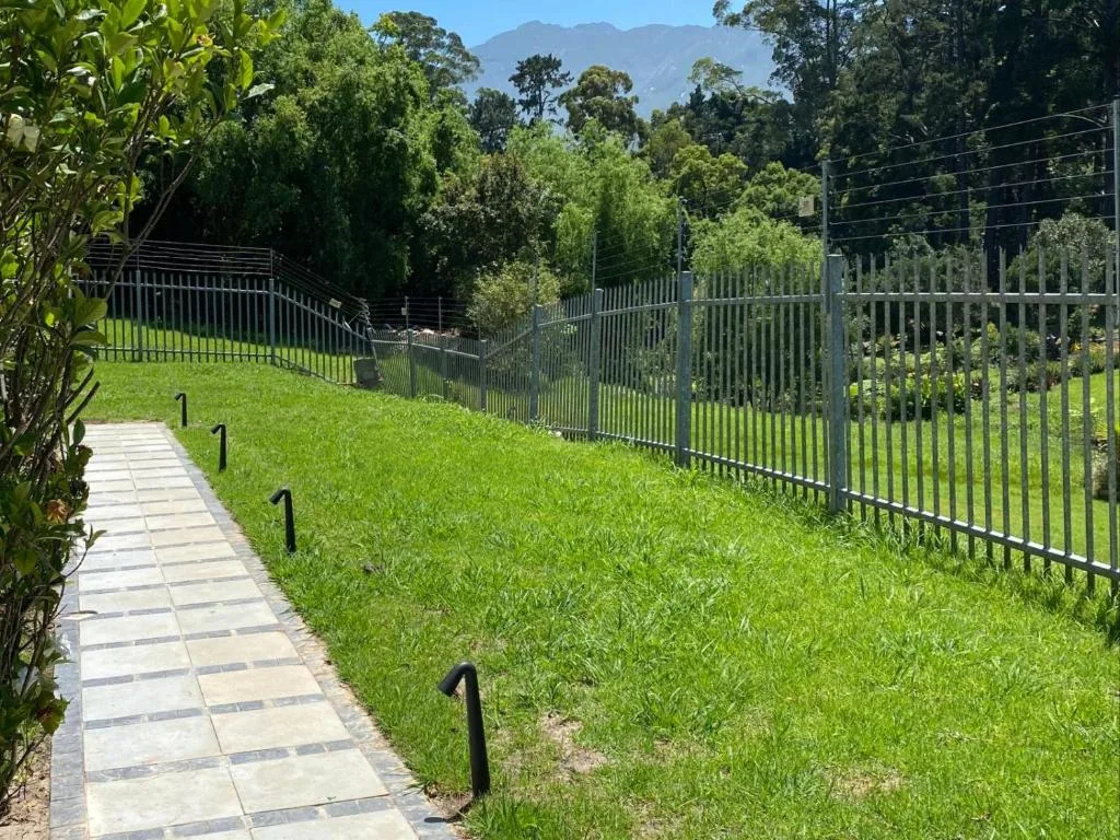 Manicured garden with paved pathway, fencing, and mountain views beyond