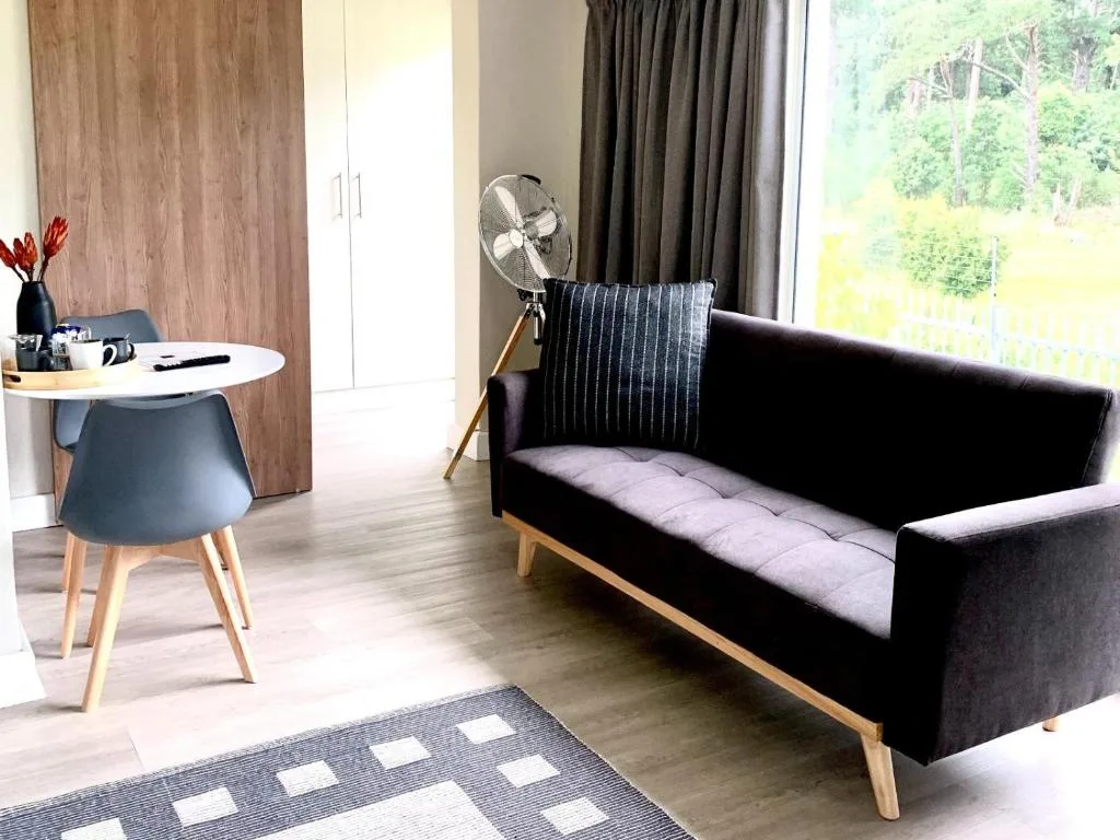 Modern lounge with black sofa, small desk, and forest views through large windows