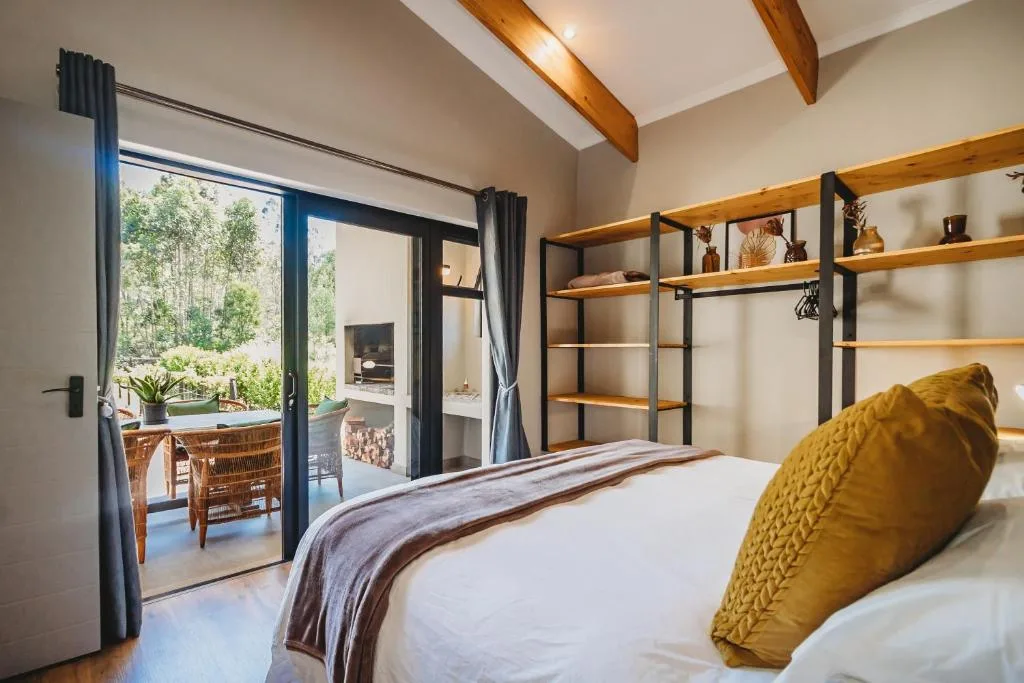 Bright bedroom with bed, wooden beams, and deck access overlooking trees