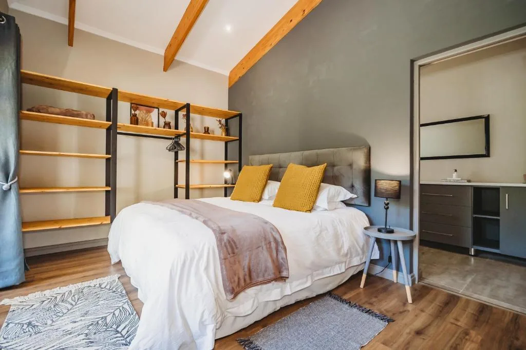 Modern bedroom with queen bed, yellow pillows, wooden beams, and ensuite bathroom