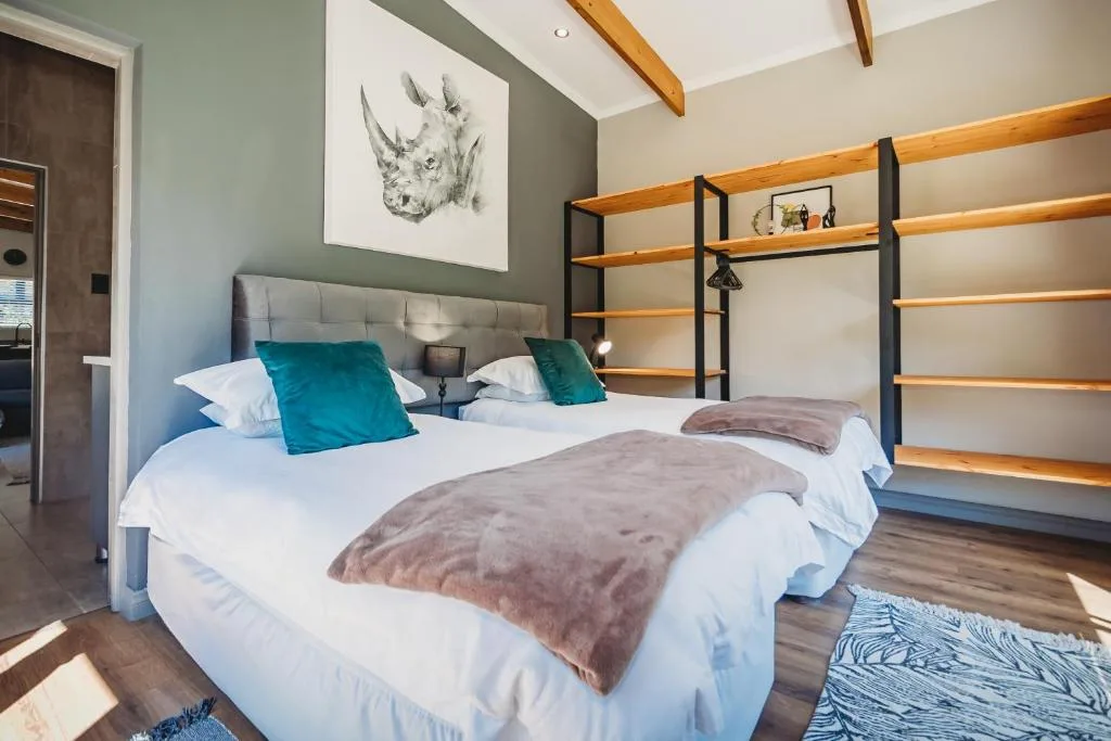 Modern bedroom with two beds, teal cushions, wooden shelving, and contemporary decor
