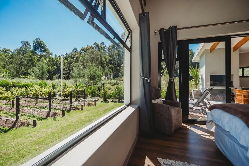Bedroom with bed overlooking vineyard gardens and forested hills through windows
