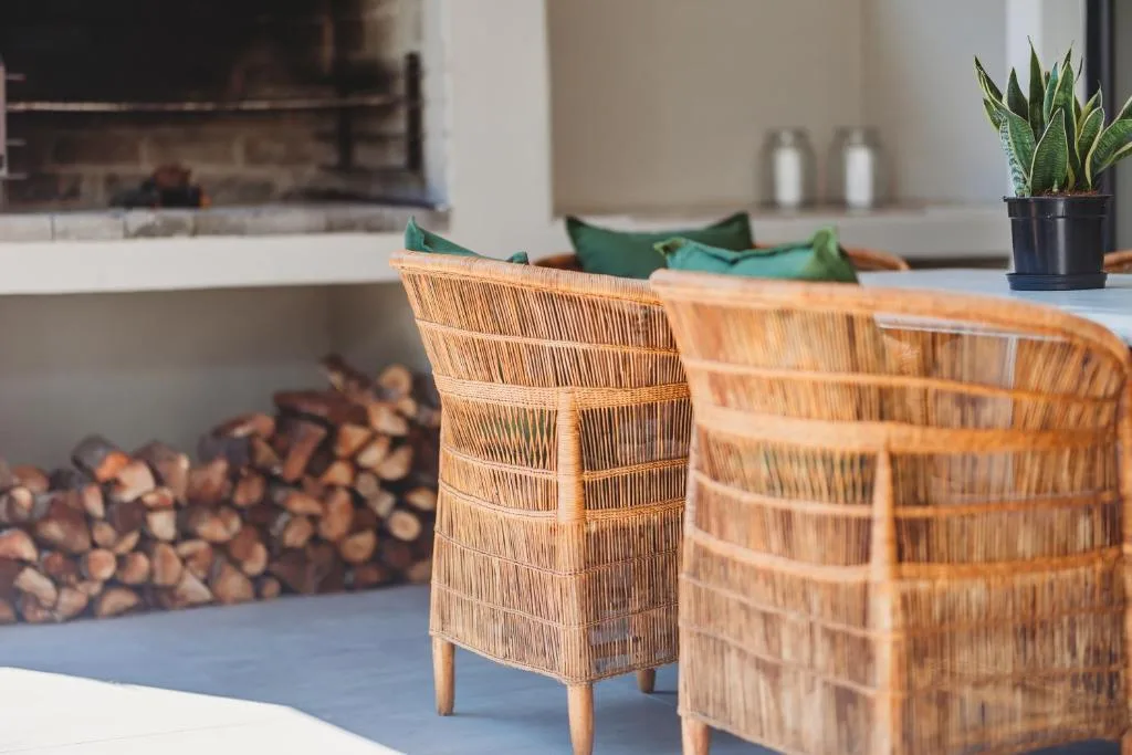Woven rattan chairs on outdoor patio with fireplace and garden plants