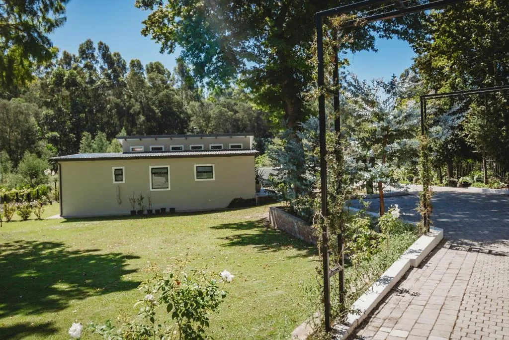 Cream-colored self-catering unit nestled among tall trees with manicured lawn