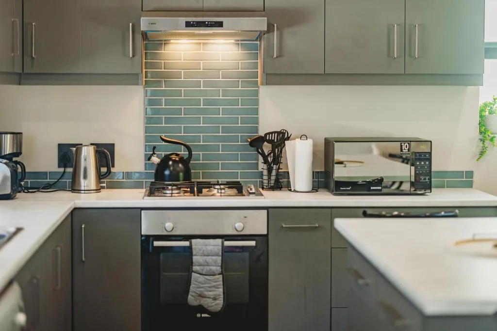 Modern kitchen with sage green cabinetry, turquoise tile backsplash, and stainless steel appliances