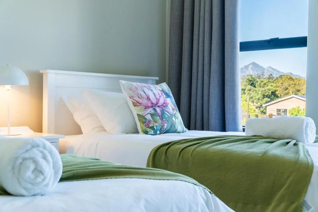 Bright bedroom with twin beds, mountain view through window, floral pillow accent