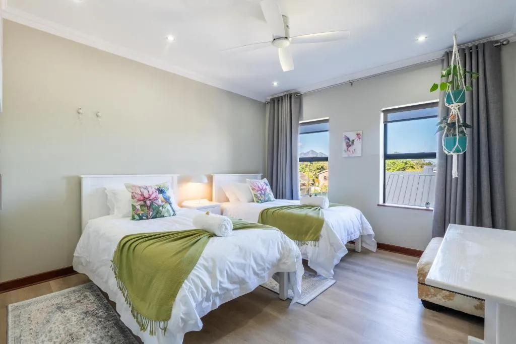 Bright twin bedroom with white bedding, green throws, and mountain views through windows