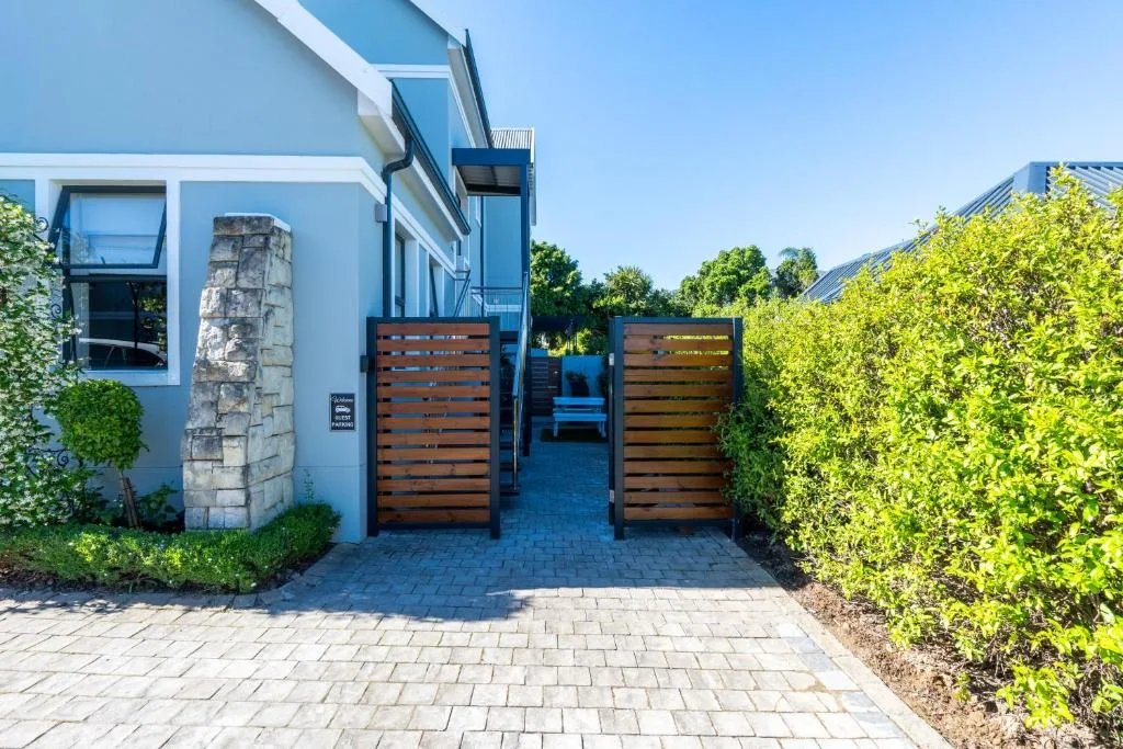 Modern blue and white building entrance with wooden gates and manicured hedges