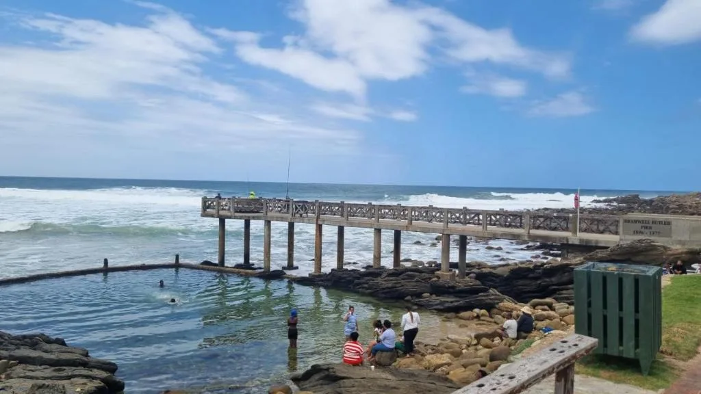 Ocean view with pier, rocky coastline, and beachgoers enjoying the water