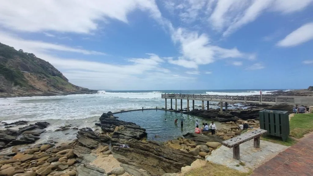 Coastal beach cove with tidal pool, wooden pier, and ocean horizon