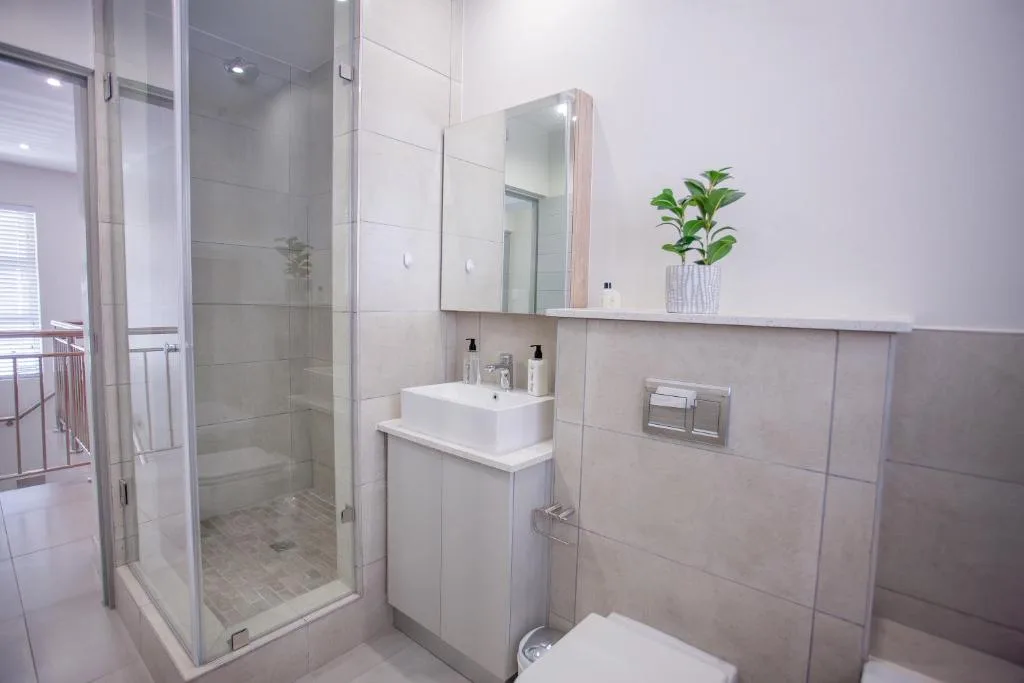 Modern bathroom with shower, vanity sink, mirror, and potted plant