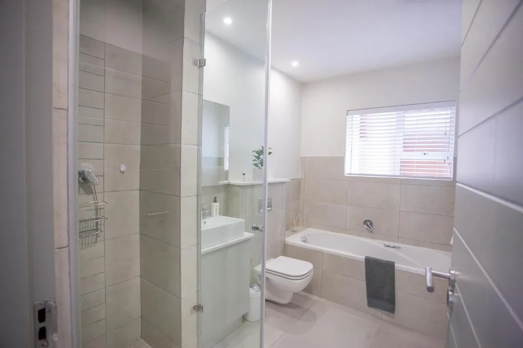 Modern bathroom with glass shower, toilet, bathtub, and window