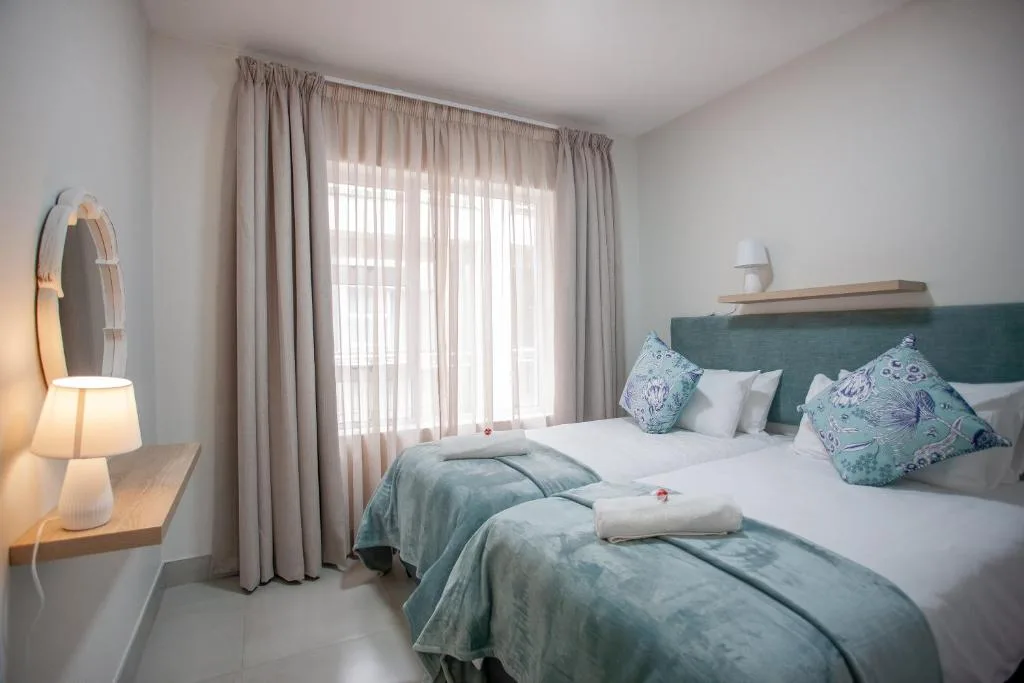 Bright bedroom with twin beds, teal headboard, and floor-to-ceiling curtains