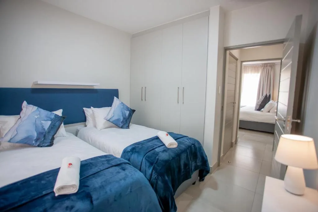 Modern bedroom with twin beds, blue velvet bedding, white wardrobe storage