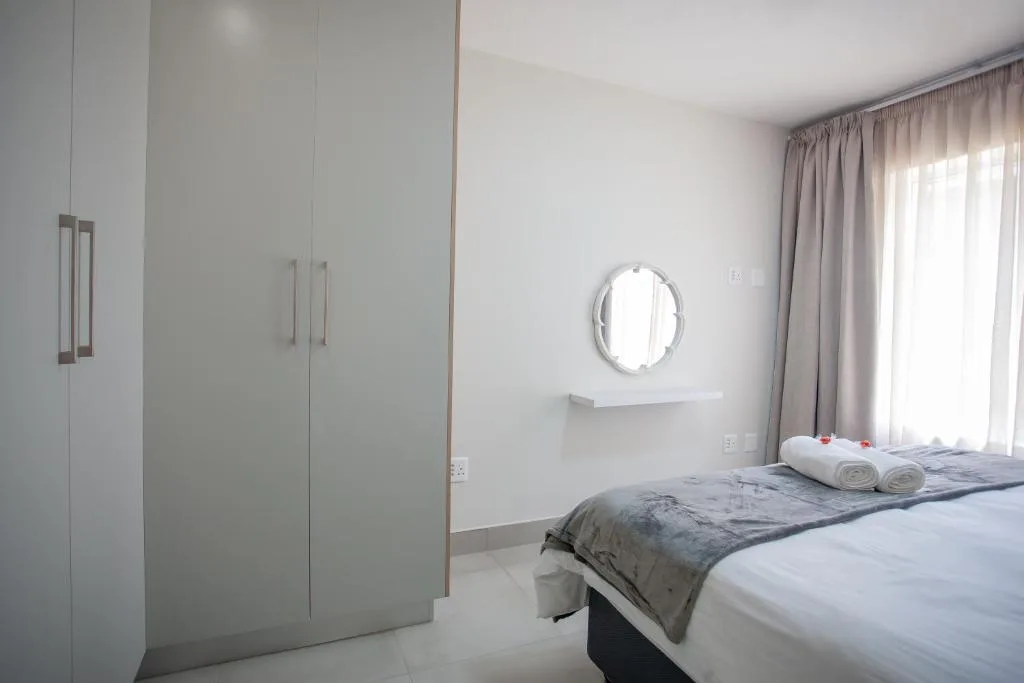 Bright bedroom with queen bed, white wardrobe, and round mirror