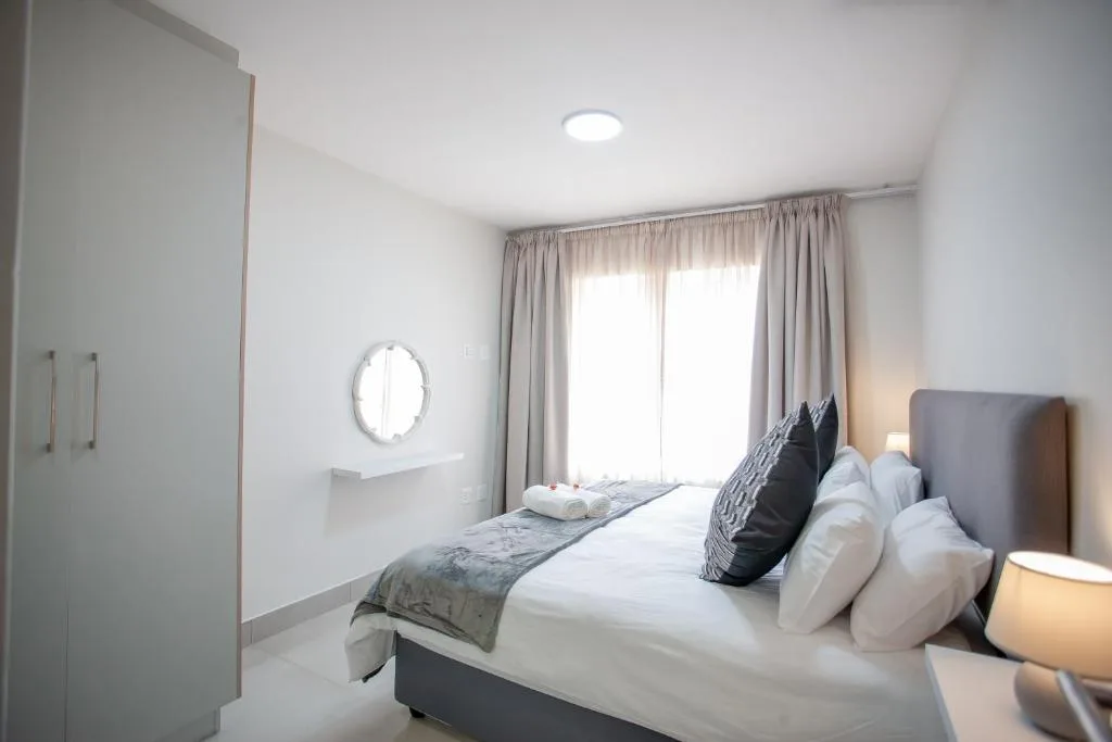 Bright modern bedroom with bed, pillows, round mirror, and garden view doors