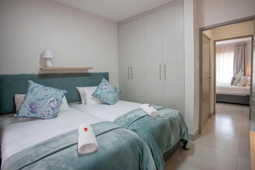 Modern bedroom with teal headboard, white bedding, and built-in wardrobes