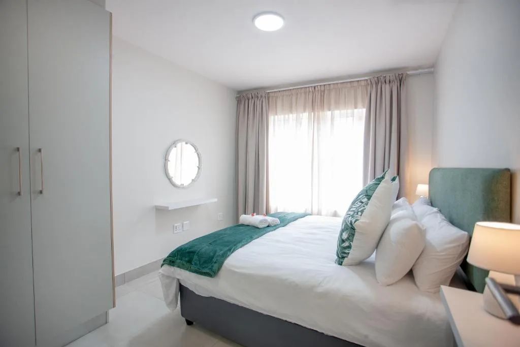 Bright modern bedroom with green upholstered headboard and white bedding