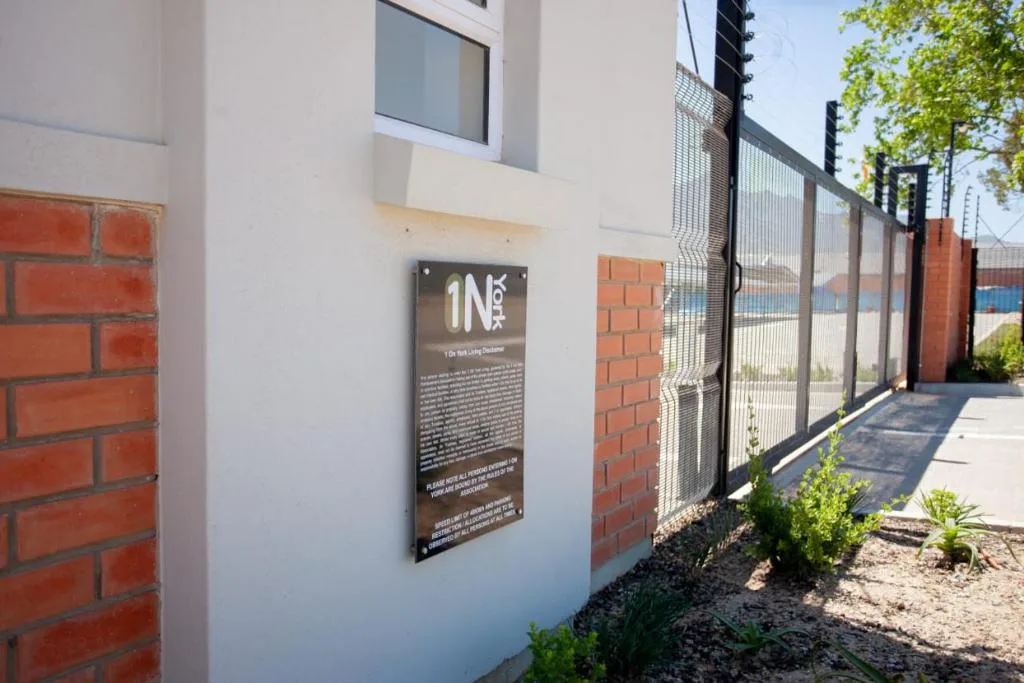 Modern white building facade with entrance plaque and secure fencing