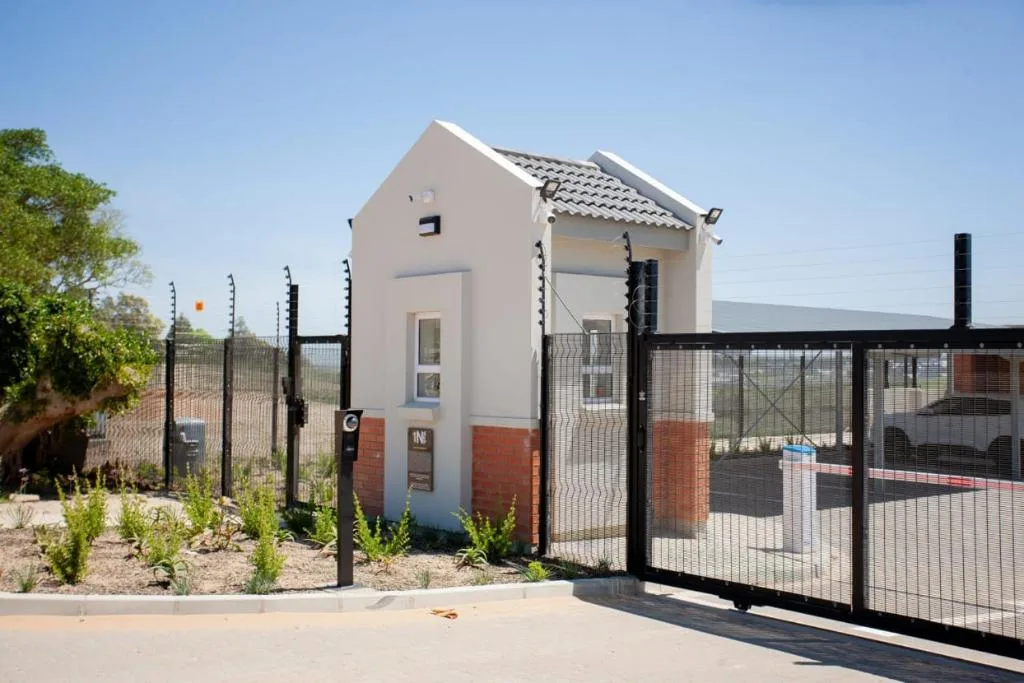 Modern white and red brick cottage with black security gate and fencing
