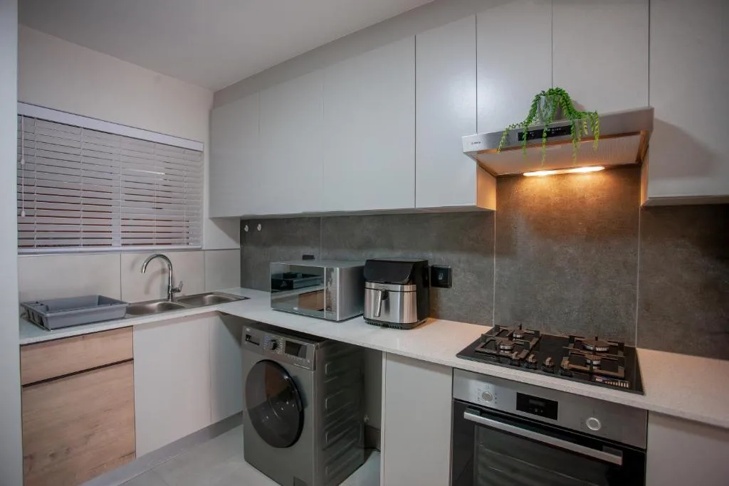 Modern kitchen with gas cooktop, oven, washing machine, and white cabinetry