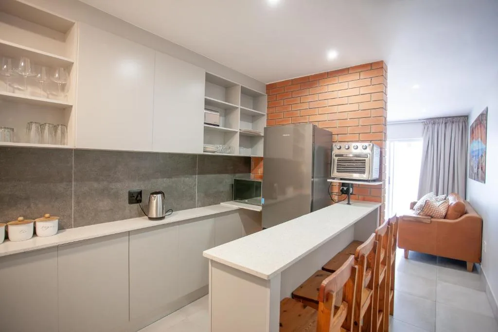 Modern open-plan kitchen with white cabinetry, stainless steel appliances, and brick accent wall