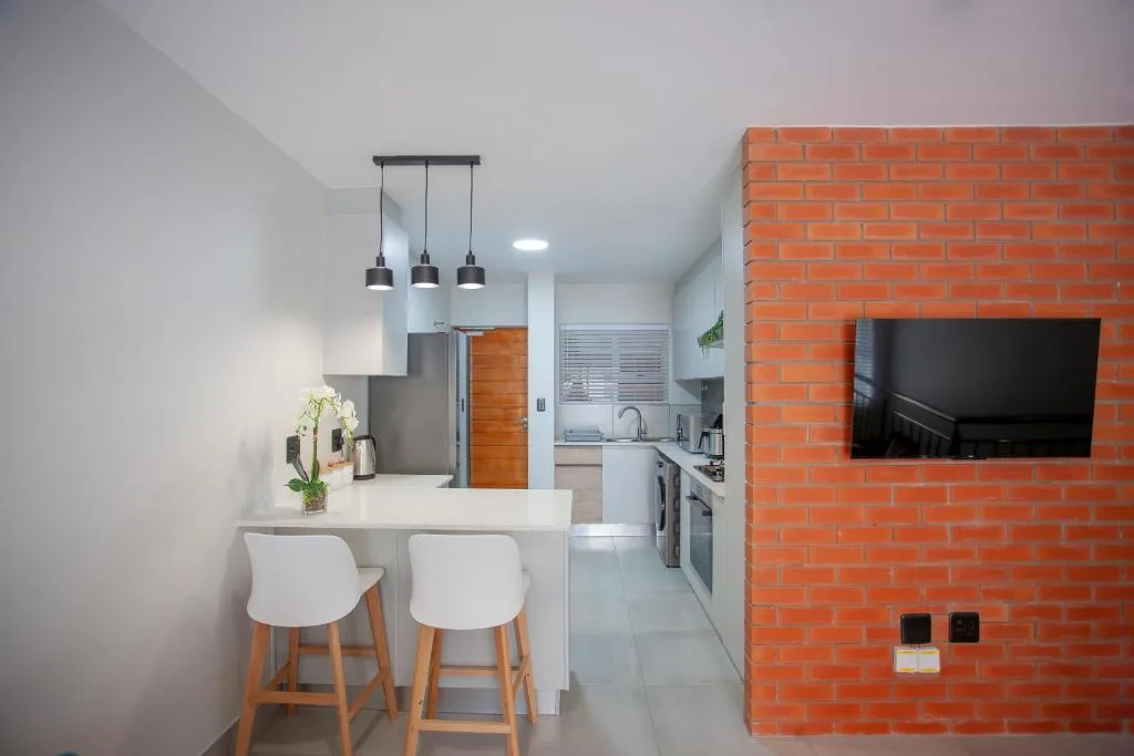Modern kitchen with white counter, bar seating, pendant lights, and stainless steel appliances