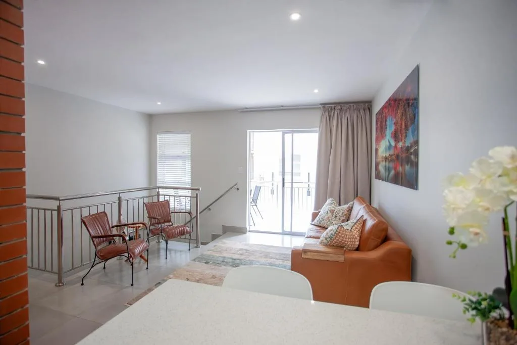 Open-plan lounge with orange sofa, seating area, and glass balcony doors