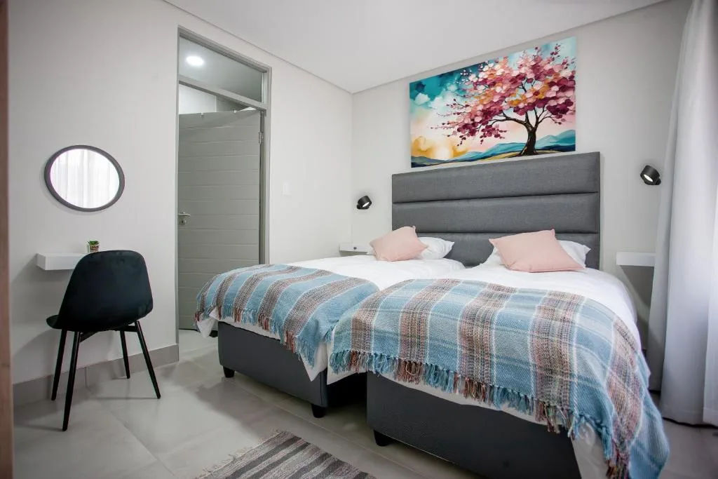 Modern bedroom with gray upholstered bed, pink cushions, and colorful tree artwork