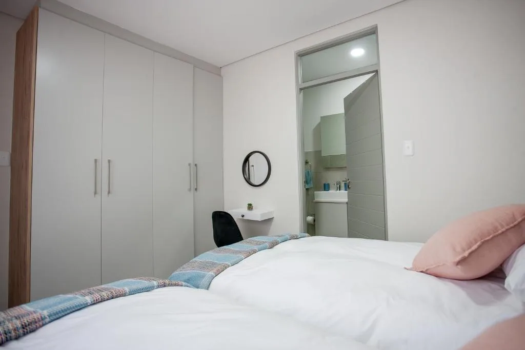 Bright bedroom with white bed, pink pillows, built-in wardrobe, and ensuite bathroom view