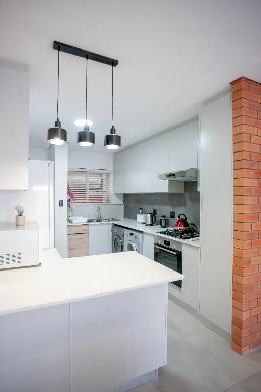 Modern white kitchen with gas stove, pendant lights, and brick accent wall