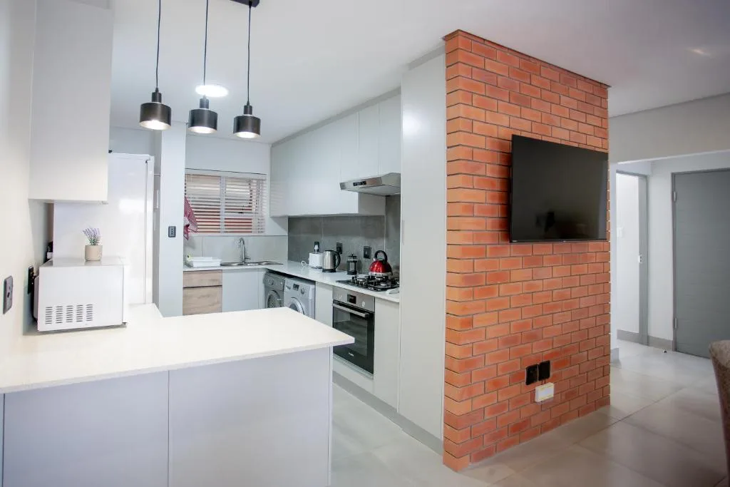 Modern kitchen with white cabinetry, stainless steel appliances, and brick feature wall