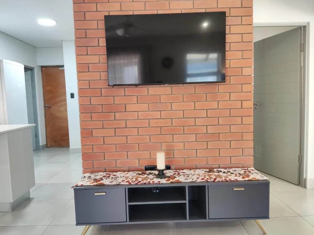 Living room with wall-mounted TV above brick feature wall and storage unit