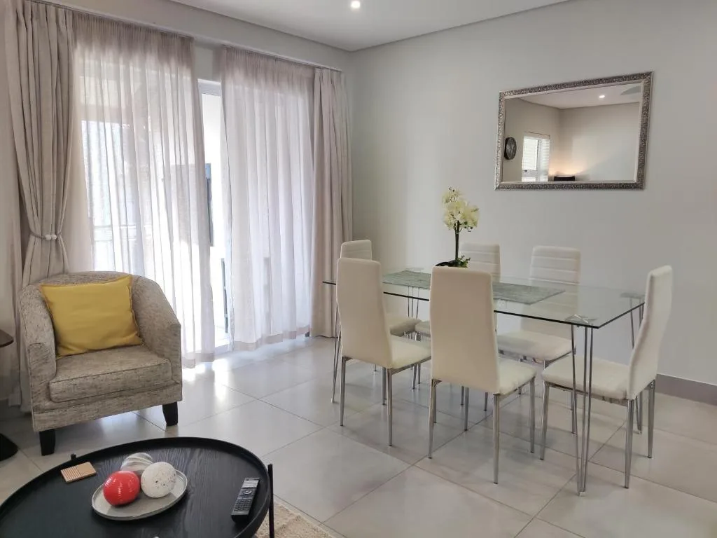 Modern lounge and dining area with armchair, glass table, and sheer curtains