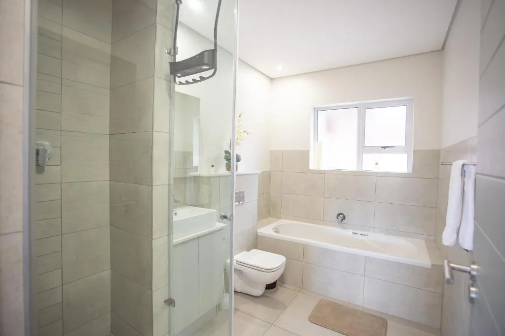 Modern bathroom with glass shower enclosure, bathtub, and toilet