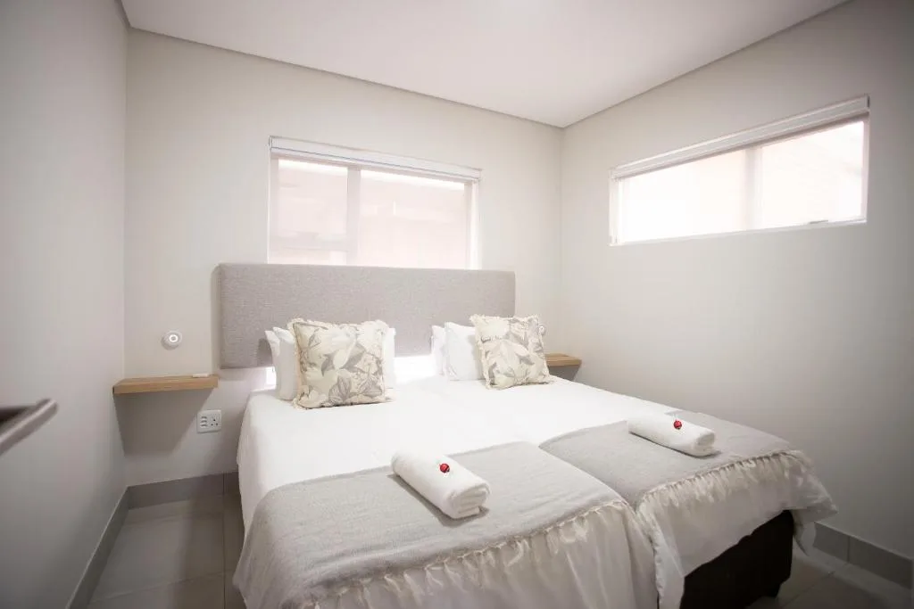 Bright bedroom with twin beds, upholstered headboard, and natural light from windows