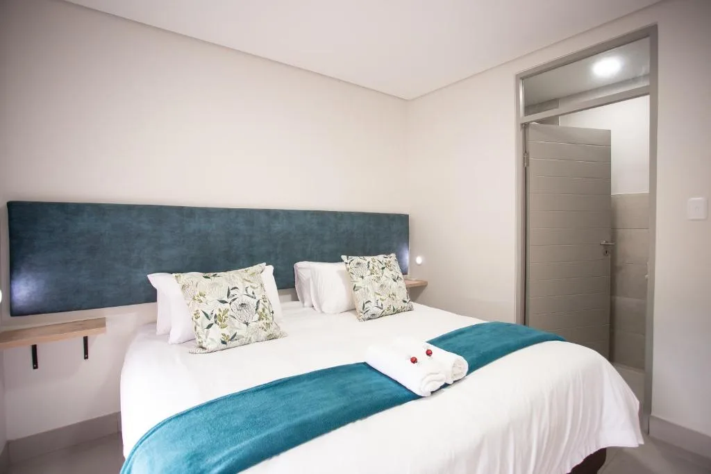 Modern bedroom with queen bed, teal headboard, and ensuite bathroom door