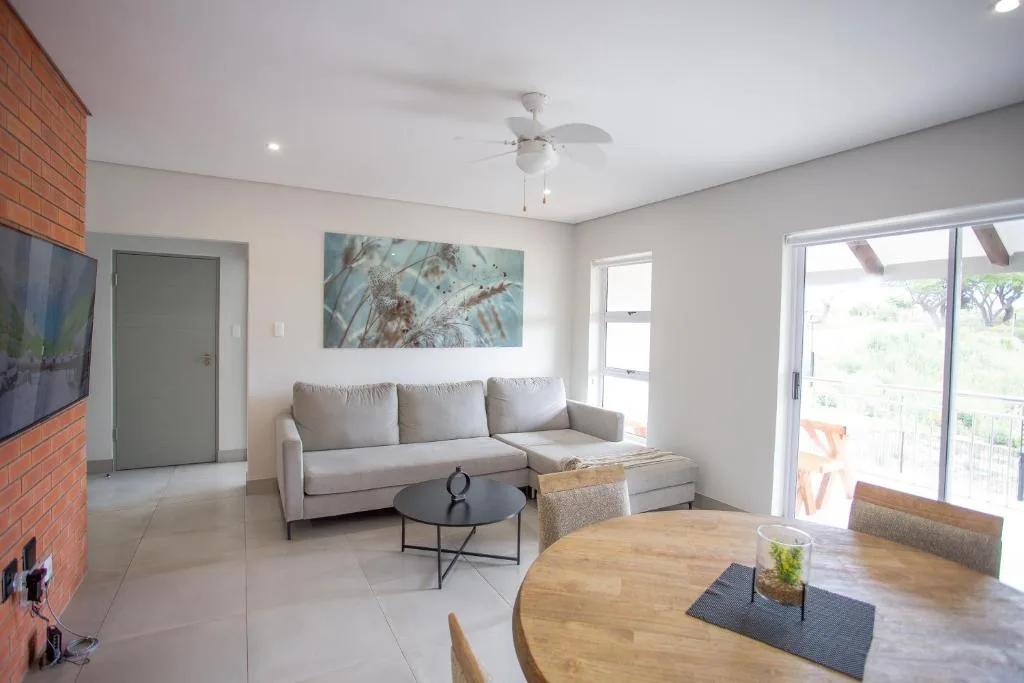 Modern lounge with grey sofa, dining table, and glass doors overlooking garden