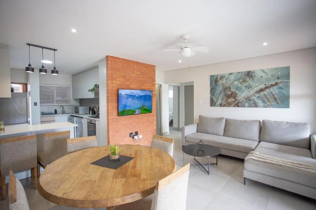 Open-plan living room with gray sofa, round wooden dining table, and brick accent wall