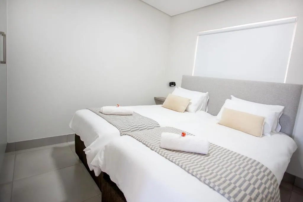 Twin beds with white linens and cream pillows, gray headboard, bright window
