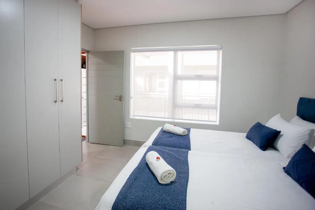 Modern bedroom with white bed, navy accents, and bright window overlooking deck