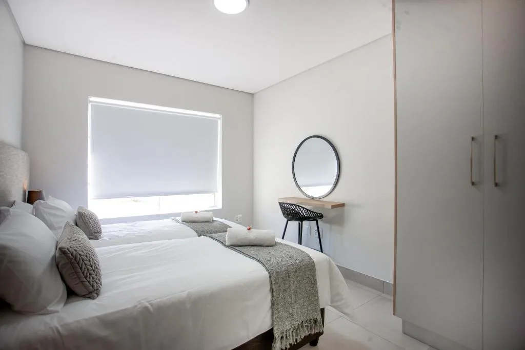 Modern bedroom with twin beds, vanity mirror, and bright window