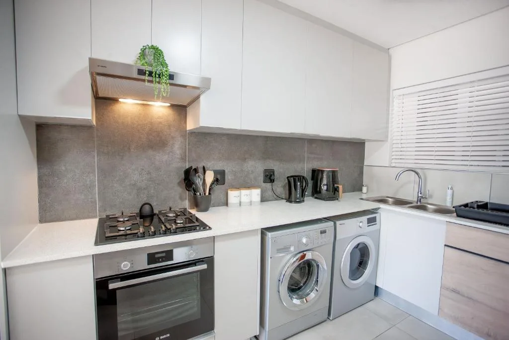 Modern kitchen with gas cooktop, oven, washing machine, and white cabinetry