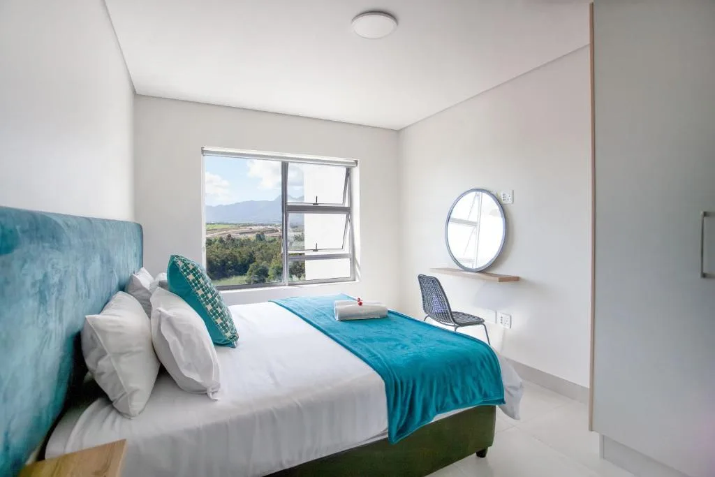 Modern bedroom with teal upholstered headboard and mountain views through window