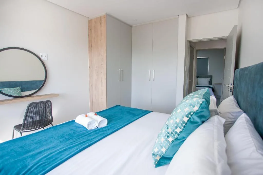 Modern bedroom with teal bedding, white pillows, and spacious built-in wardrobes