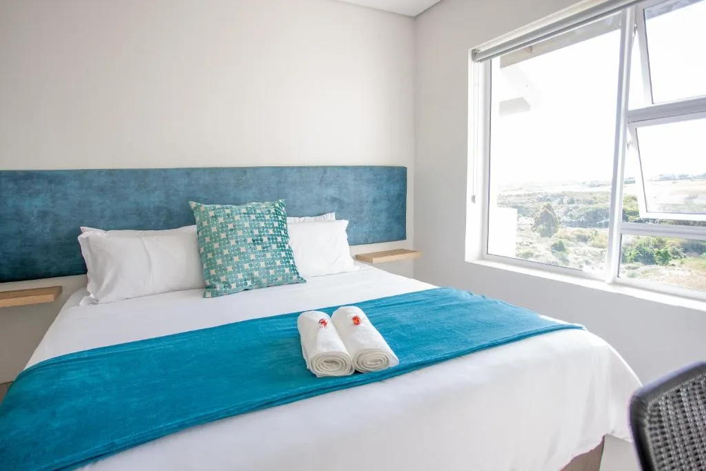 Modern bedroom with blue headboard, white bedding, and scenic landscape views