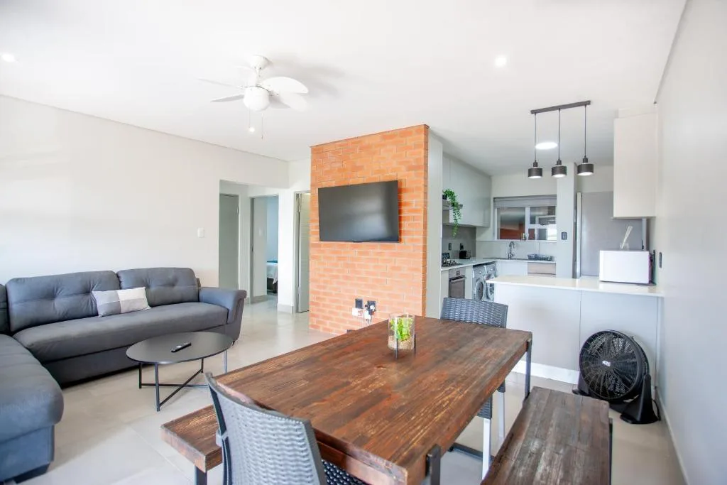 Open-plan living area with dark sofa, wooden dining table, and TV feature wall