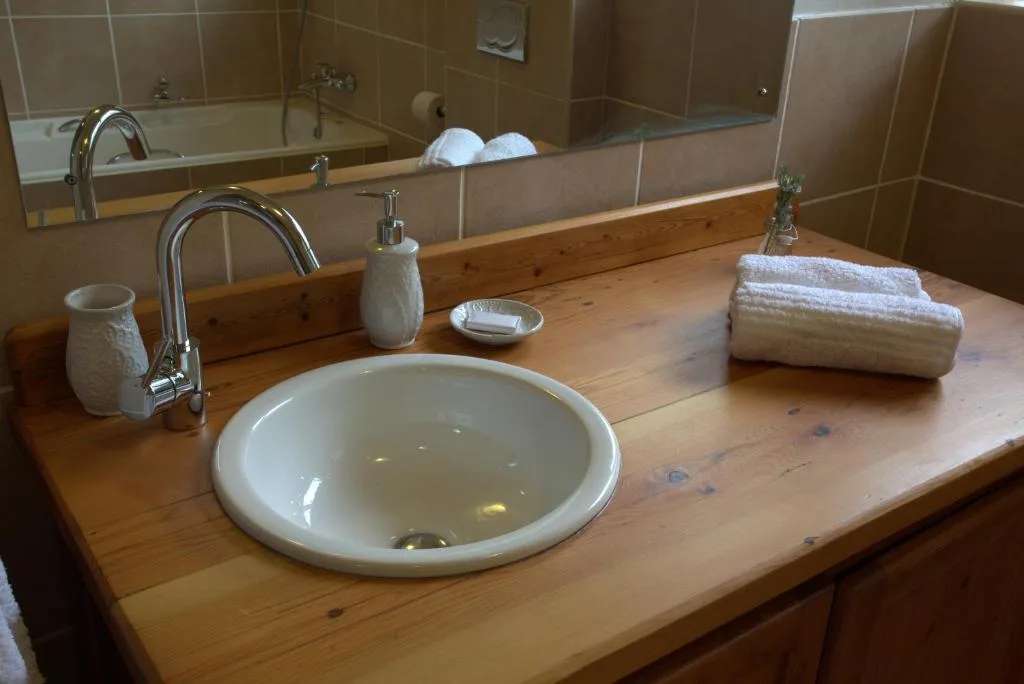 Wooden vanity with round basin sink and chrome faucet, folded towels nearby